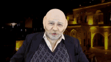 a man with a bald head and a mustache is standing in front of a building at night