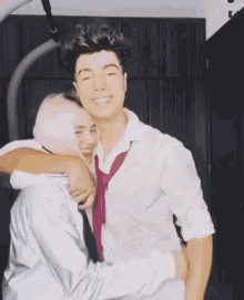 a man in a white shirt and tie is hugging a woman in a hijab