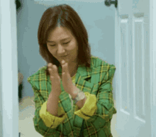 a woman in a green and yellow plaid jacket is clapping her hands in a room .