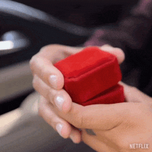 a woman is holding a red box with a ring inside of it .