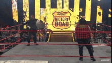 two men in a wrestling ring with a sign that says victory road in the background
