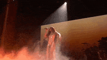 a woman singing into a microphone on a stage with smoke coming out of it