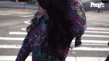 a woman in a colorful dress is crossing a street in front of a sign that says " people "