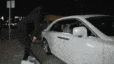 a man standing next to a white car that has the letter s on it