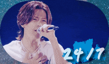 a man singing into a microphone with the number 24/7 in the background