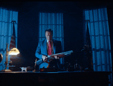 arnold schwarzenegger in a blue suit and red tie holding a sword