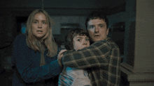 a man in a plaid shirt is hugging a woman and a child