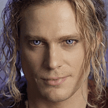 a close up of a man with long blonde hair and blue eyes