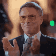 a man in a suit and tie is clapping his hands while wearing sunglasses .