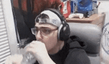 a man wearing headphones and glasses is drinking from a bottle .