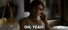 a man in a white tank top is talking on a cell phone and the words oh yeah are above him