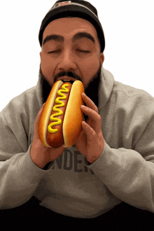 a man with a beard is eating a hot dog that has mustard on it
