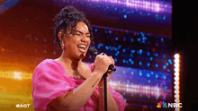 a woman in a pink dress is singing into a microphone on nbc