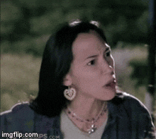 a woman wearing a heart shaped earring and a necklace looks surprised
