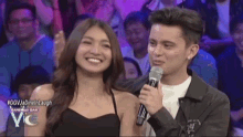 a man and a woman are standing next to each other while a man holds a microphone .