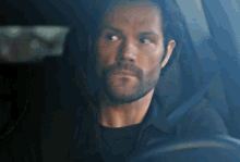 a man with a beard is sitting in a car and looking out the window