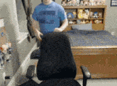 a man in a blue shirt that says ' cube ' on it stands in front of a chair