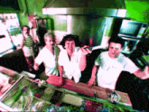 a group of people are standing in a kitchen and one of them is wearing a white shirt that says ' a '