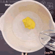 a pot of water is being poured into a bowl of yellow liquid