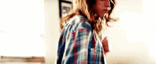 a woman in a plaid shirt is standing in front of a window in a room .