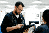 a man with a stethoscope around his neck looks at a tablet while a woman looks on