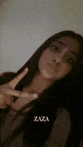 a girl with long dark hair is giving a peace sign and has the name zaza on the bottom