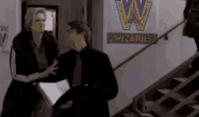 a man and a woman are standing next to each other in front of a sign that says `` wizards '' .