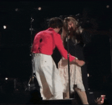 a man in a red shirt and white pants is standing next to a woman in a white dress on a stage