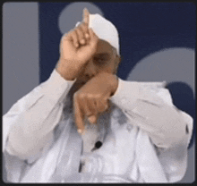a man wearing a white hat and a white shirt is making a gesture with his hand