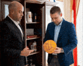 two men looking at a water polo ball in front of a cabinet