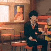 a man in a suit sits at a table in front of a poster of a woman drinking beer
