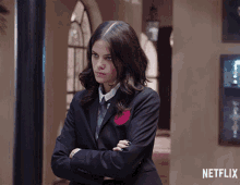 a woman in a suit and tie is standing with her arms crossed in front of a wall that says netflix on it