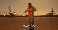 a man in a helmet and safety vest is standing on an airport runway .