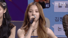 a woman is singing into a microphone while standing in front of a speech bubble .