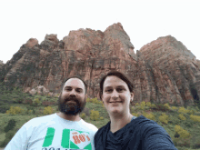 a man and woman are posing for a picture in front of a mountain
