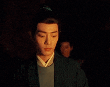 a man in a kimono is standing in the dark with his eyes closed and his hair in a bun .