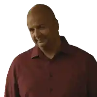 a bald man in a maroon shirt looks down at something