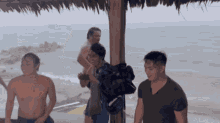 a group of men are standing under a thatched roof near the ocean
