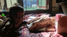 a little girl is laying on a bed next to a pink box that says ' a ' on it
