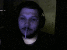 a man wearing headphones is smoking a cigarette in a dark room with a blue light behind him