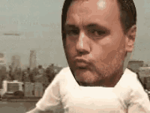 a man with a baby 's head on his chest is making a funny face in front of a city .