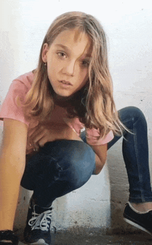 a young girl squatting down wearing a pink shirt