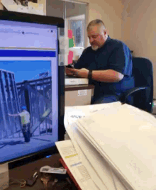 a man sits at a desk looking at his phone in front of a computer monitor