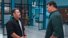 two men are standing next to each other in an office talking to each other .