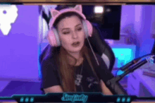 a woman wearing pink headphones and a cat ear headband is sitting in a chair in front of a microphone .
