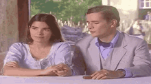 a man and a woman are sitting at a table holding hands and looking at something .