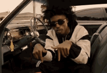 a man wearing sunglasses sits in the driver 's seat of an old car