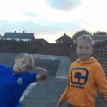 a boy wearing an orange carhartt sweatshirt stands next to another boy