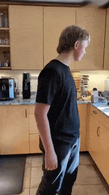 a man in a black shirt is standing in a kitchen near a coffee maker
