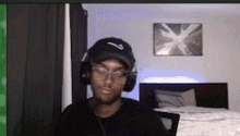 a man wearing headphones and a baseball cap is sitting in a bedroom .